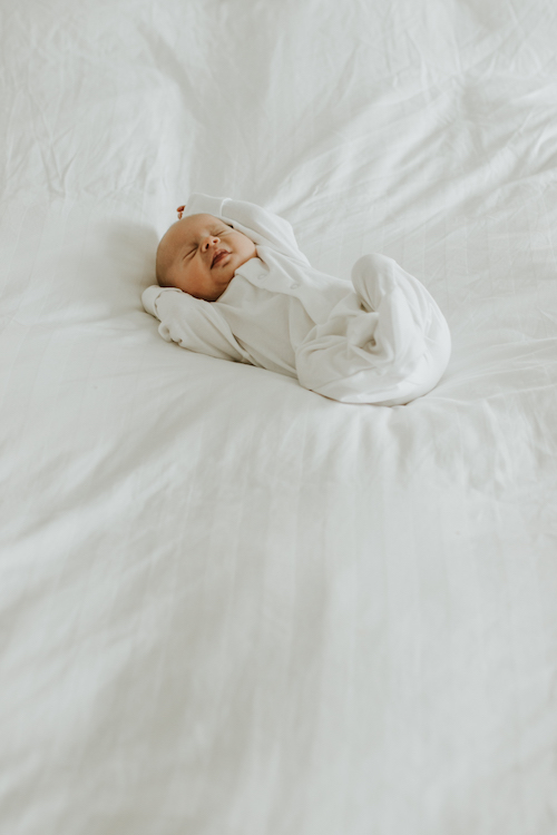 Newborn baby wearing white onesie on bed | Baby Photographer in Banbury, Oxford, Buckingham, Bicester and Aylesbury