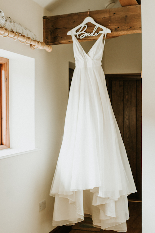 Bridal gown hanging from oak beam | Natural wedding photography in Buckinghamshire