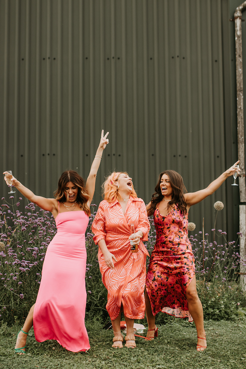 Three wedding guests all wearing different shades of pink and red dresses