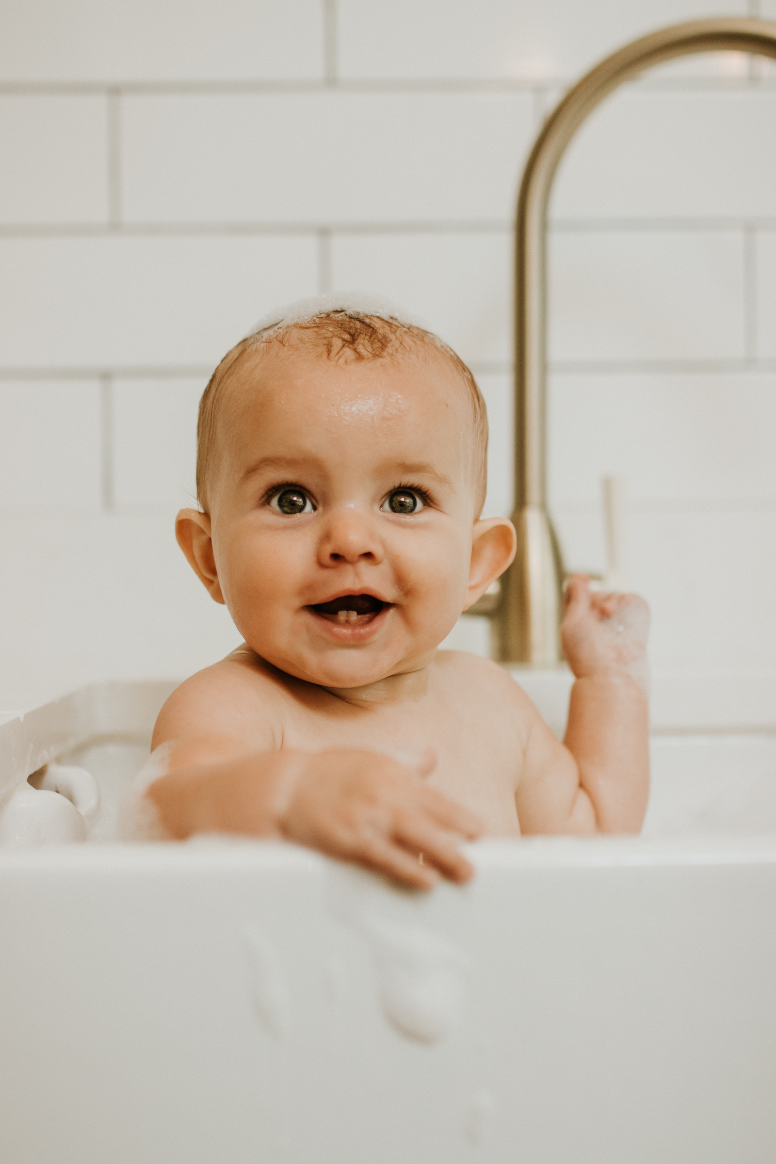 Baby having a sink bath in the kitchen and smiling at the camera