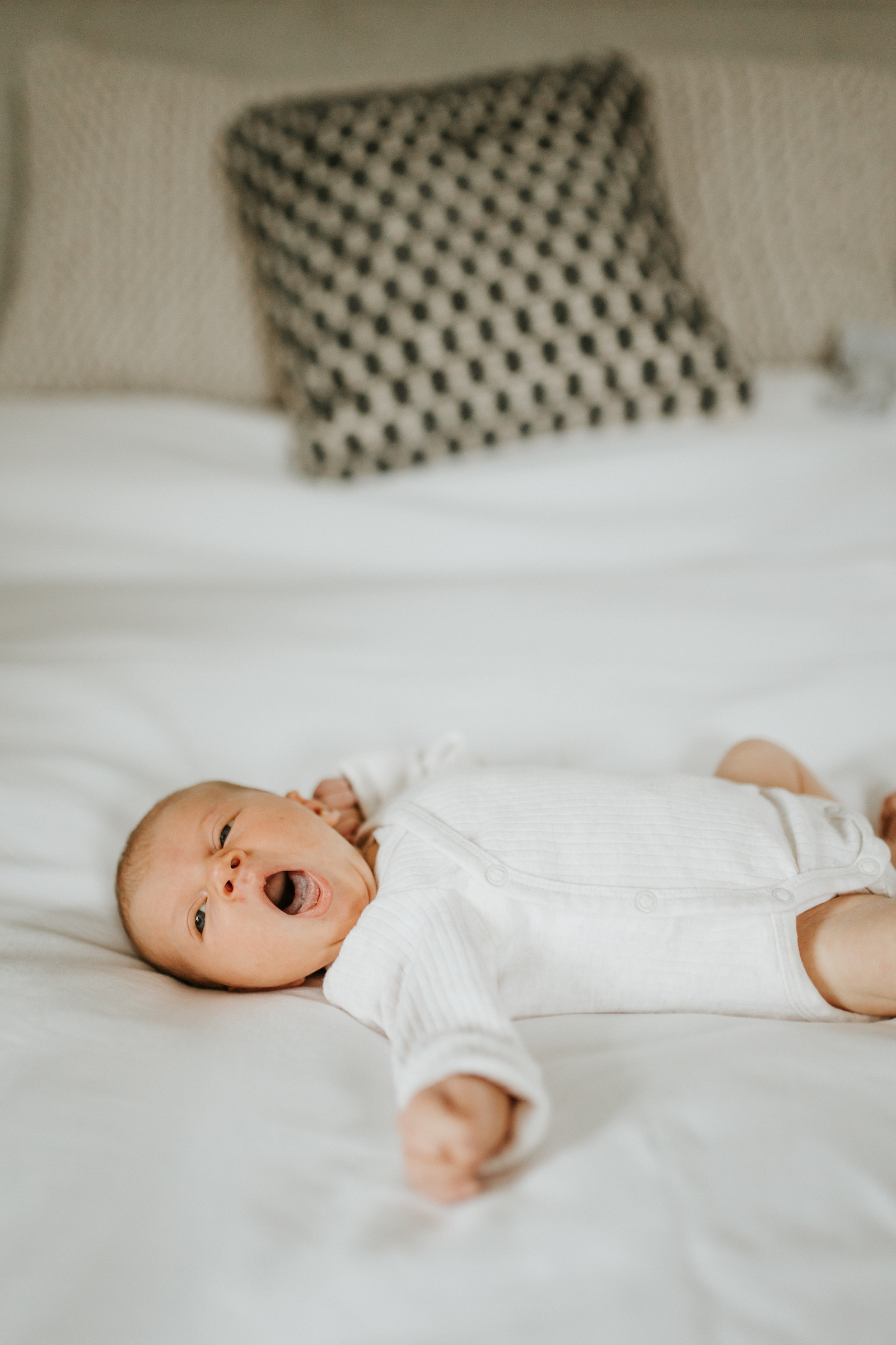 Newborn baby in white onesie yawning